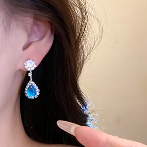 Close-up detail of silver earrings with a blue teardrop stone and white zircons