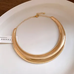 Dettaglio di un girocollo in metallo dorato lucido a forma di mezzaluna su un piatto bianco