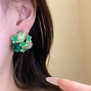 Detailed close-up showing a green butterfly stud earring with stones on a model ear