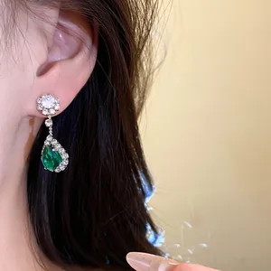 Close-up detail of an elegant green teardrop earring with diamond zircon on a model