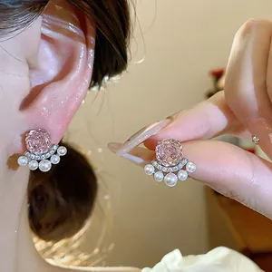 Close-up detail of elegant pink flower zircon and pearl stud earrings worn on model ear.