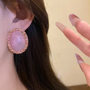 Close-up of a vintage-style pink oval acrylic earring with rhinestone border being worn.