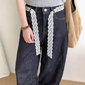 Close-up of white floral lace ribbon used as a decorative belt on dark denim jeans