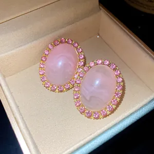 Macro detail view of vintage pink oval acrylic stud earrings with rhinestone halo in box