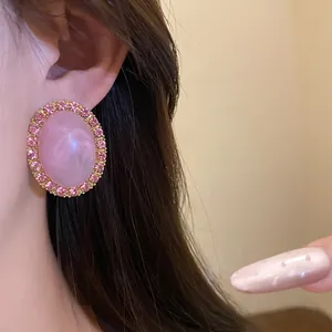 Detailed view of pink oval vintage stud earring with rhinestone halo on model's ear