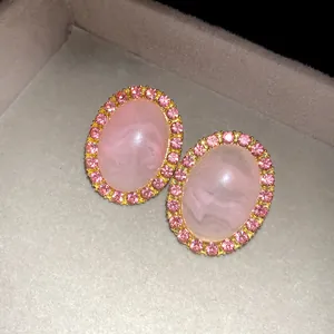 Close-up of pink oval acrylic earrings with rhinestone border in a grey jewelry box.