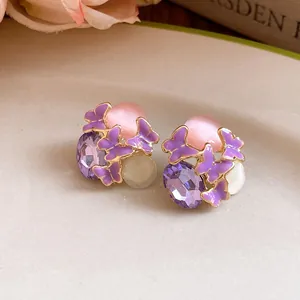 Close-up of purple butterfly stud earrings with crystal and pink cat-eye stones.