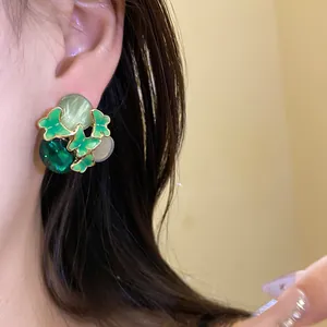 Close-up detail of green enamel butterfly stud earrings with cat-eye stones shown on ear
