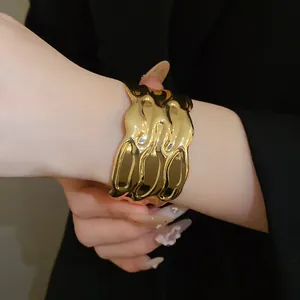 Detailed view of a wide vintage gold cuff bracelet with wavy texture on a model's arm