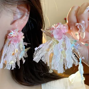 Dettaglio di orecchini a fiore in resina rosa con nappe di nastri colorati e aghi d'argento.