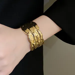 Detailed macro view showing the gold wavy textured metal cuff bracelet on woman's wrist