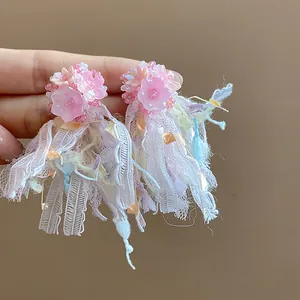 Dettaglio ravvicinato di orecchini a fiore in resina rosa con nappe di pizzo multicolore