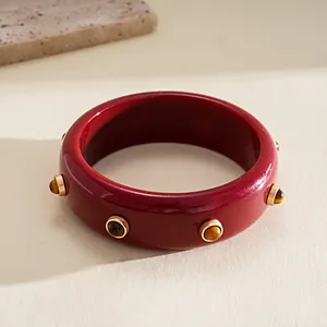 Detail of a retro burgundy resin bangle decorated with golden studs and tiger eye stones