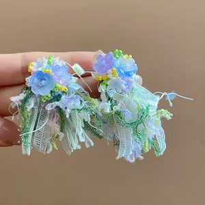 Primo piano di orecchini a fiore in resina con nastro colorato e nappe di pizzo