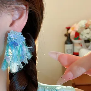 Dettaglio ravvicinato di orecchino a perno con fiore in resina blu e nappine in nastro colorato