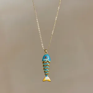 Dettaglio del ciondolo a forma di pesce in smalto blu e oro su catena in acciaio