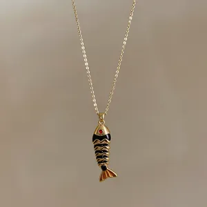 Dettaglio macro di una collana con ciondolo a pesce in acciaio dorato e smalto nero fine
