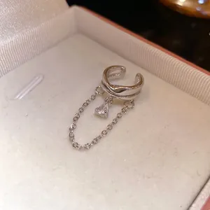 Macro view of a silver ear cuff with a dangling pear-shaped zirconia and chain detail.