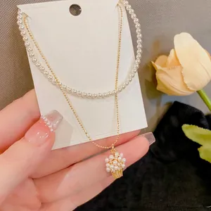 Primo piano della collana a due strati con filo di perle e ciondolo a cesto di fiori.