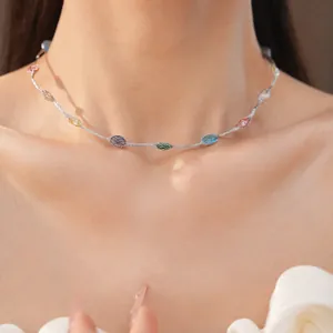 Detail van een delicate zilveren ketting met kleurrijke zirkoonstenen op de hals van een model