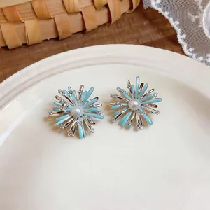 Close-up of zircon enamel firework stud earrings with a pearl center on a white plate.