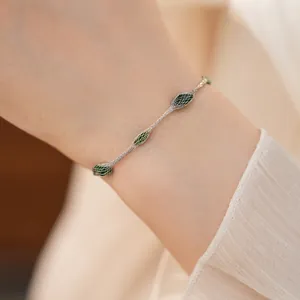 Elegante close-up van een zilveren mesh armband met groene bladvormige bedeltjes om pols