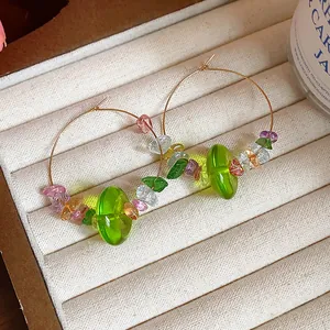 Vue détaillée des perles de résine verte et pierres colorées sur créoles dorées élégantes