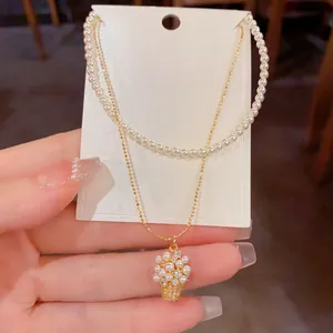 Dettaglio del pendente a cesto di fiori su collana a doppio strato di perle dorate.