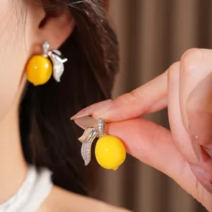 Vista detallada de pendientes de limón de resina con elegantes detalles de hojas de circonio