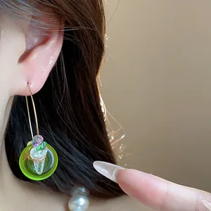 Détail de boucles d'oreilles créoles en résine verte avec des perles colorées au modèle