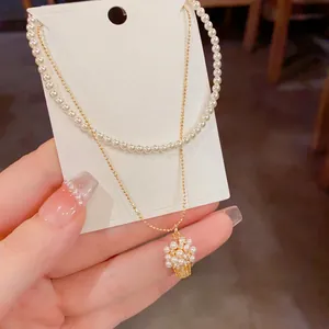 Elegante collana a due strati con girocollo di perle e raffinato ciondolo a cestino.