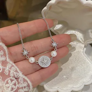 Elegante bracciale in argento con ciondoli a stella e perle bianche su sfondo conchiglia.