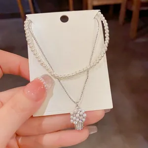 Primo piano di collana a doppio strato con perle e ciondolo a forma di cesto di fiori.