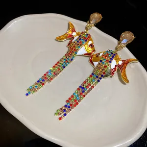 Nahaufnahme von bunten Strass-Fisch-Ohrringen mit Fransen auf einem Keramiktablett