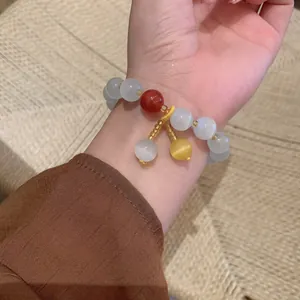 Elegant beaded cat-eye stone bracelet with red and yellow charms worn on female wrist