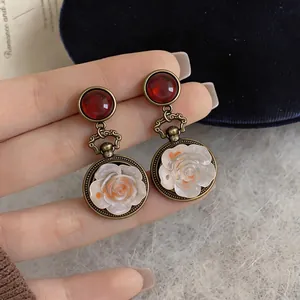 Dettaglio macro di orecchini a goccia vintage con rosa in resina e finitura oro antico