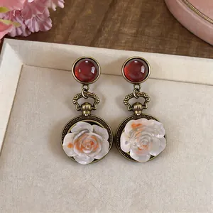 Primo piano di orecchini vintage a rosa in resina con perni cabochon rossi e finitura bronzo.