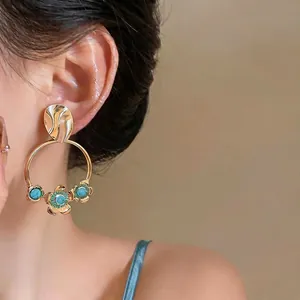 Exaggerated vintage gold round hoop earrings with turquoise floral accents on model's ear.