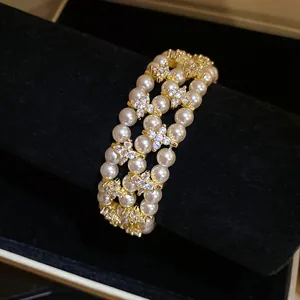 Macro detail of triple-layer pearl bracelet with sparkling zircon flower charms.