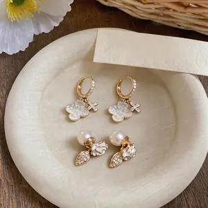 Elegant gold plated earrings featuring pearl and floral charms on a cream display plate