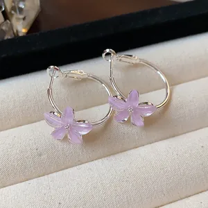 Detailed macro view of elegant purple resin flower hoop earrings on a beige velvet tray