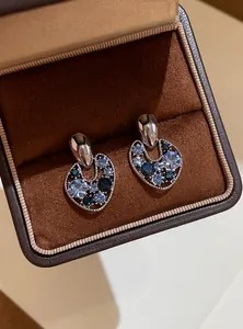 Macro view of blue rhinestone earrings displayed in a brown velvet jewelry box.