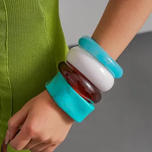 Vista dettagliata di bracciali impilati in resina sfumata nei toni blu, bianco e ambra