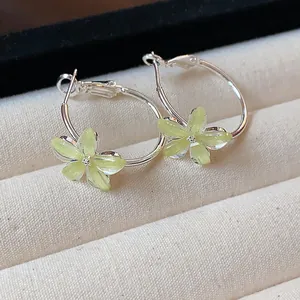 Detailed shot of silver hoop earrings with yellow-green resin flowers on a display tray.