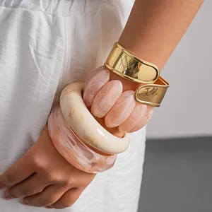 Close-up view of stacked marbled acrylic bangles and a wide golden metal cuff