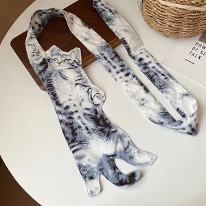 Détail d'un collier écharpe original avec imprimé chat gris sur table blanche.