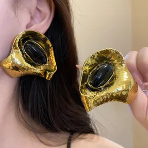Gros plan de boucles d'oreilles vintage en or avec une texture froissée et résine noire