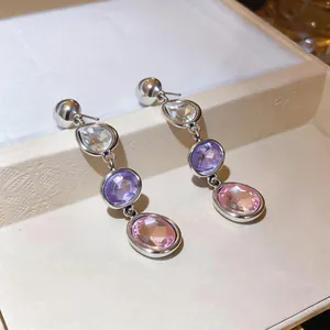 Close-up of silver drop earrings with faceted purple and pink crystals.