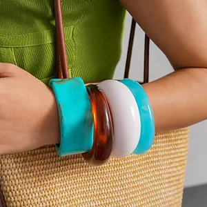 Primo piano di quattro braccialetti in resina colorata indossati sul polso con borsa di paglia