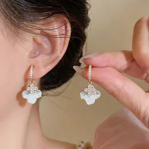 Elegant four-leaf clover earrings with white inlay and shimmering crystals in detail view.